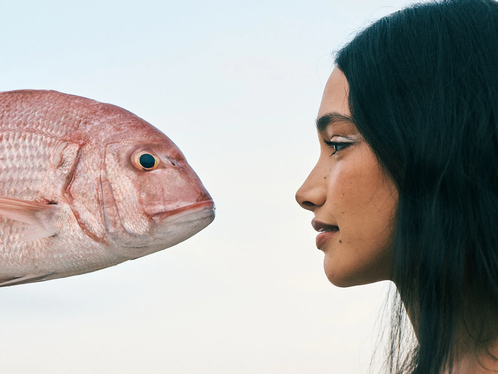 A fresh fish and a woman face each other on the beach.